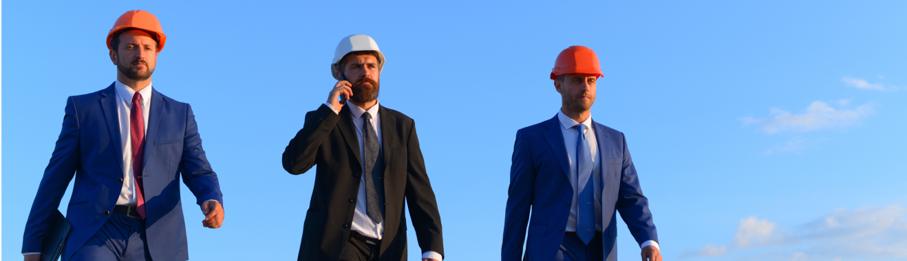 Engineers and architects in formal suits, holding black and brown briefcases, wearing white and orange helmets, walking confidently under a blue sky. One person talks on the phone, embodying a professional business and construction concept